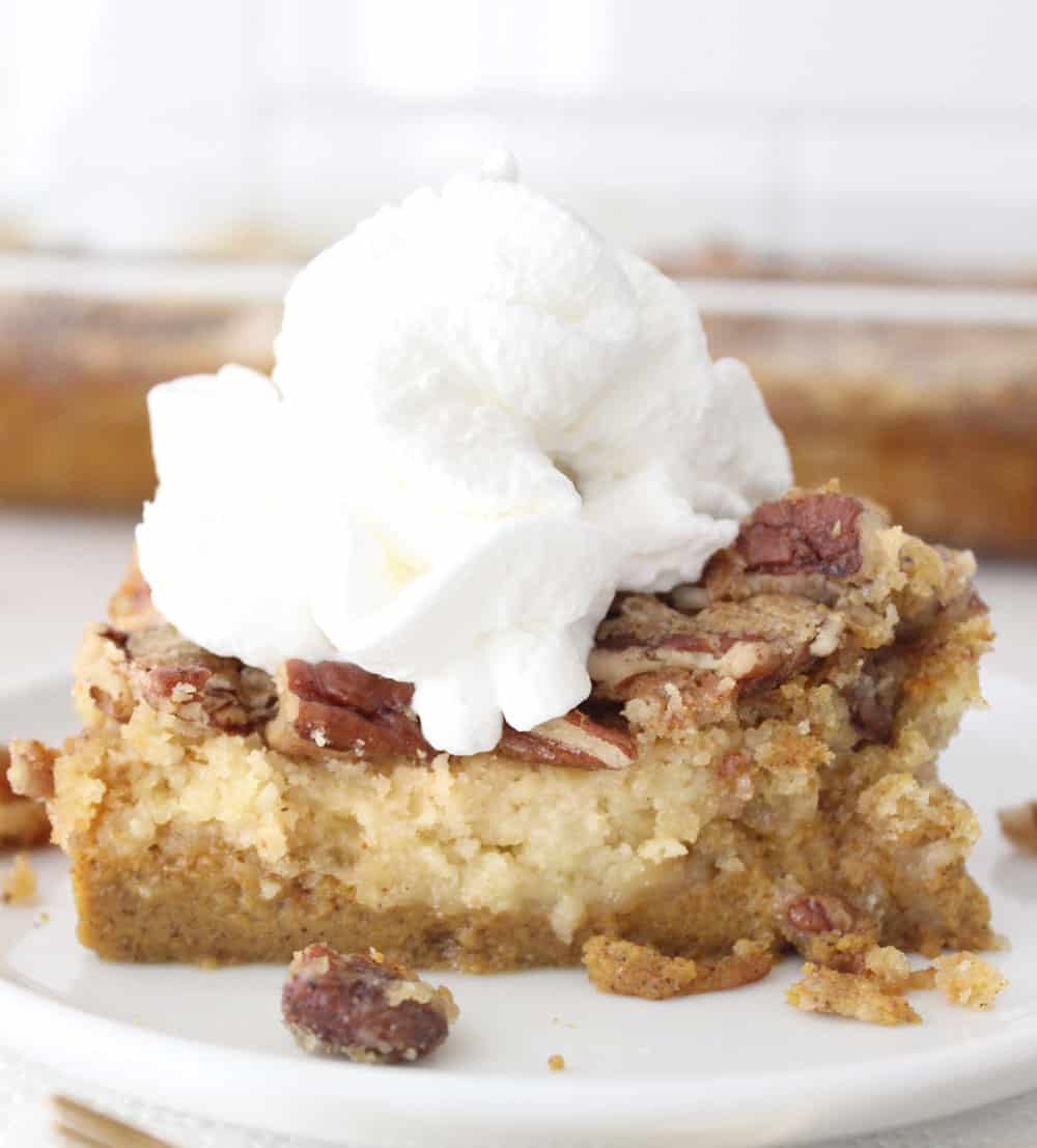 Pumpkin dump cake on a white plate, crushed walnut topping and a big dollop of whipped cream on top.