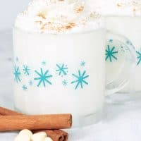 White Hot Chocolate in mugs with whipped cream and cinnamon. White chocolate chips on the side of the mugs.