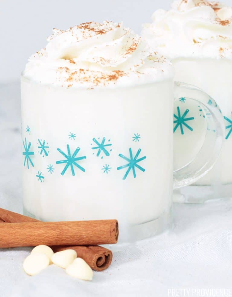 White Hot Chocolate in mugs with whipped cream and cinnamon. White chocolate chips on the side of the mugs.