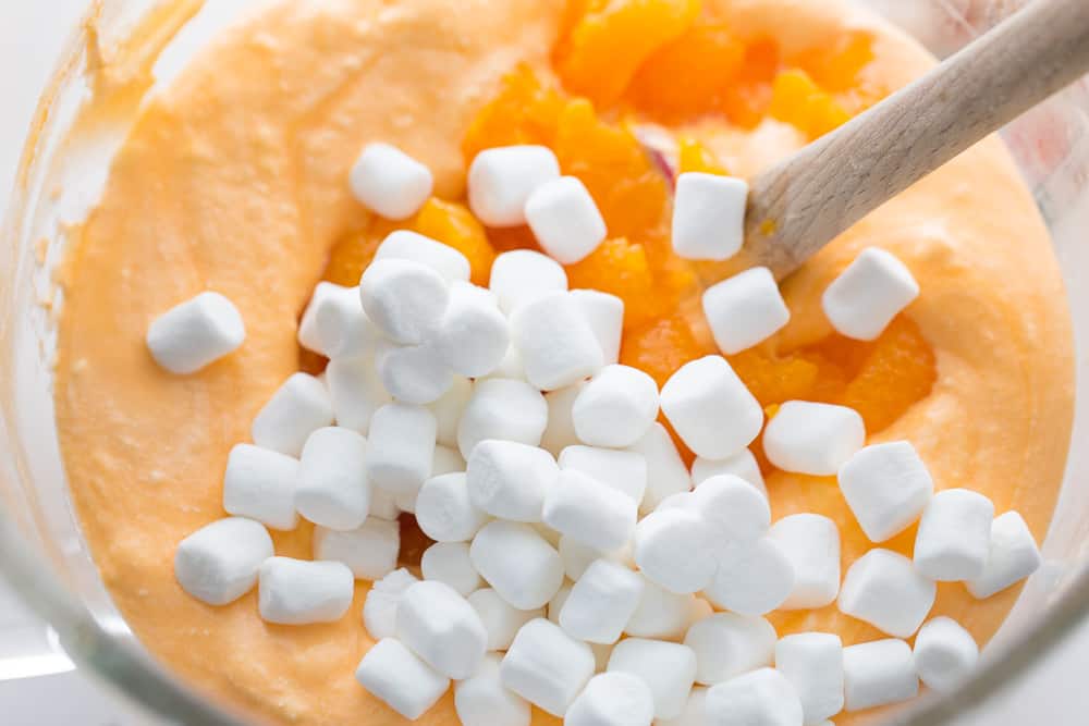mixing together ingredients for orange fluff in a glass bowl with a wooden spoon