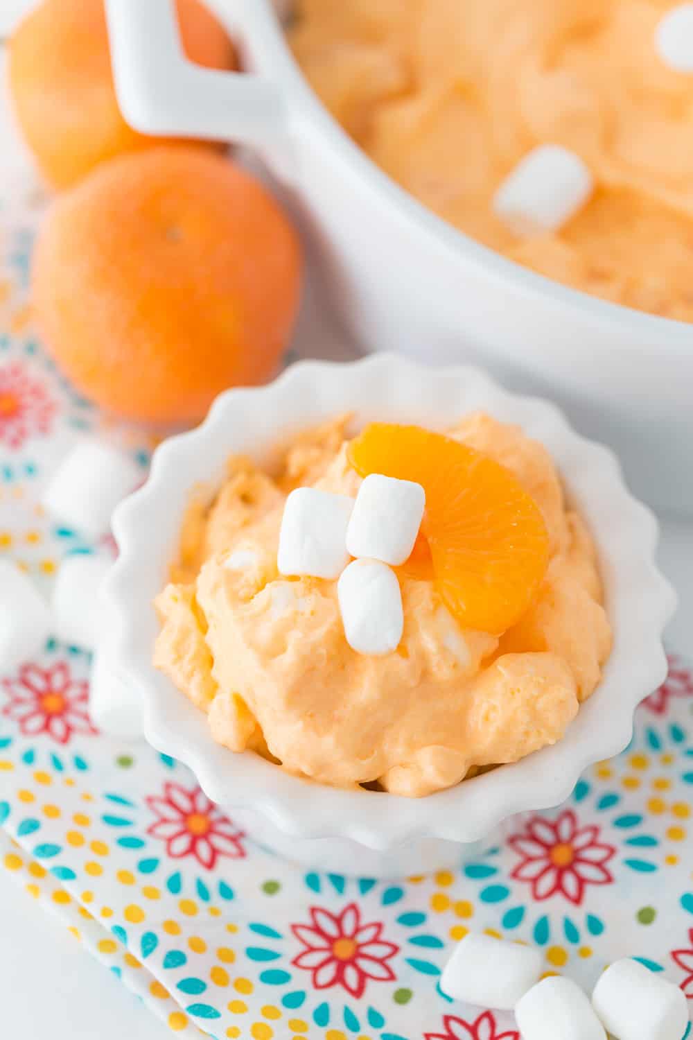 close up of orange dreamsicle salad with marshmallows on top and oranges in the background