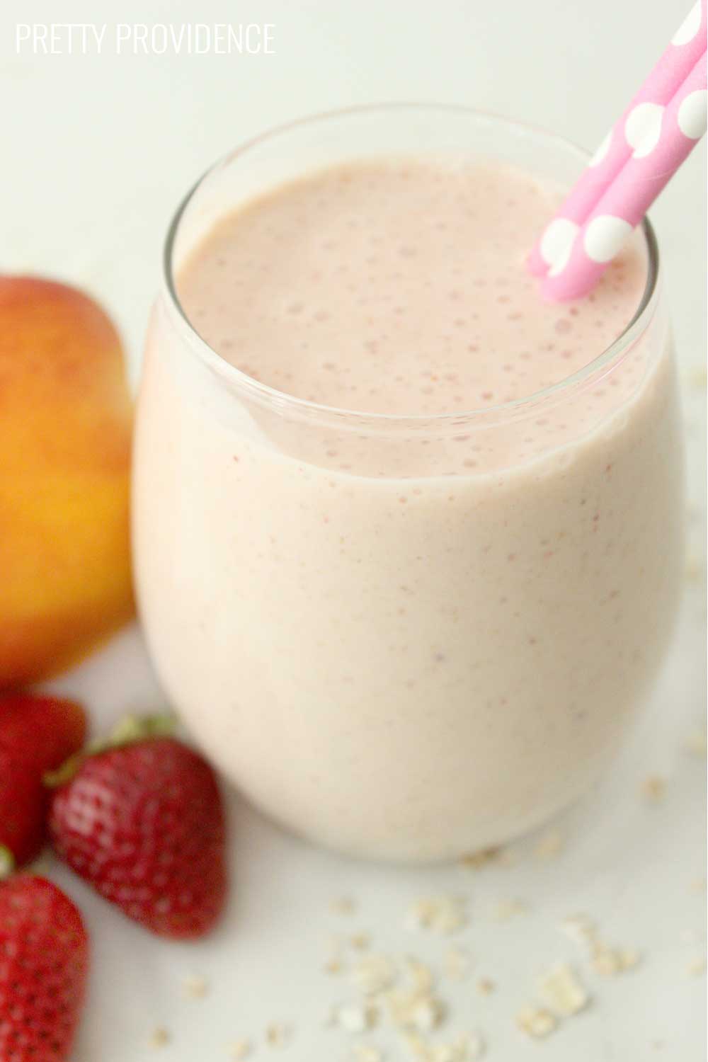 Strawberry peach smoothie in a clear glass with two pink polka dot straws sticking out. 