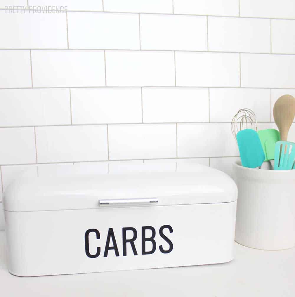 Cricut vinyl word 'CARBS' on a white bread box in kitchen.