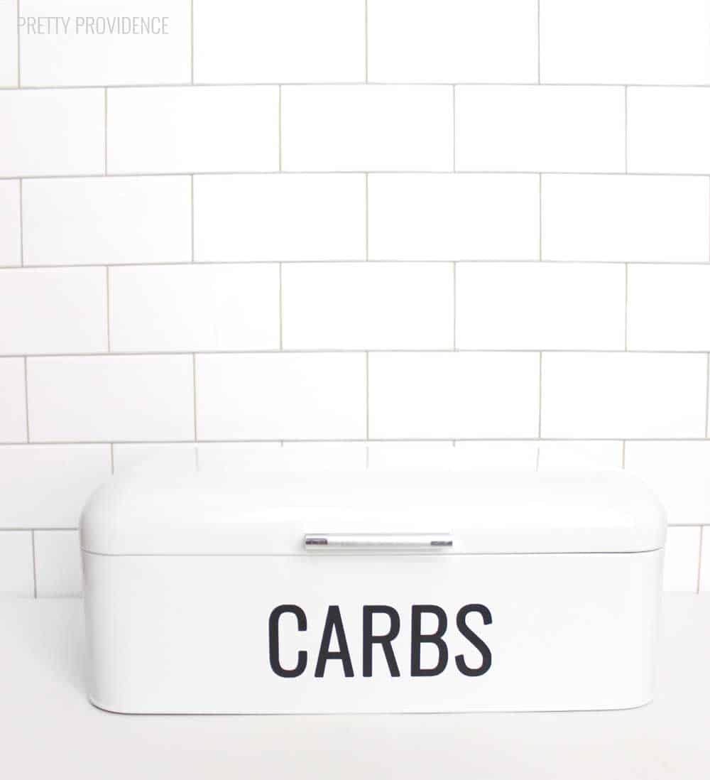 Cricut vinyl word 'CARBS' on a white bread box in kitchen.