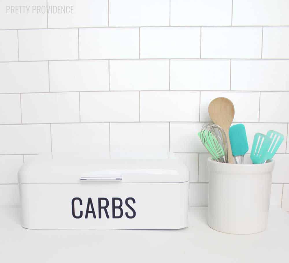 Cricut vinyl word 'CARBS' on a white bread box in kitchen.