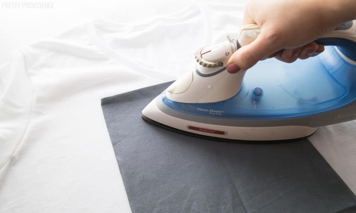 Blue and white iron over a sheet of fabric ironing a white t-shirt