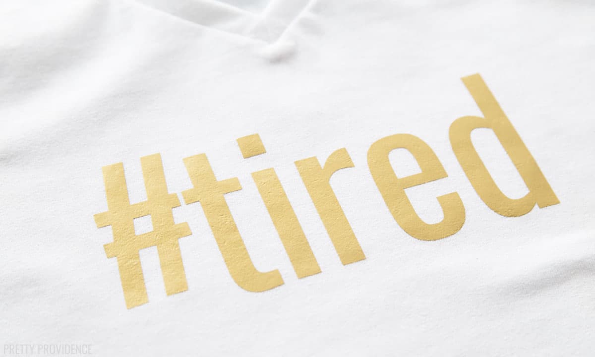 "#tired" in gold iron-on vinyl on a white t-shirt