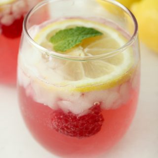 Fresh raspberry lemonade in a clear glass with lemon and mint.