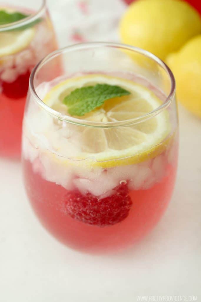 Fresh raspberry lemonade in a clear glass with lemon and mint.