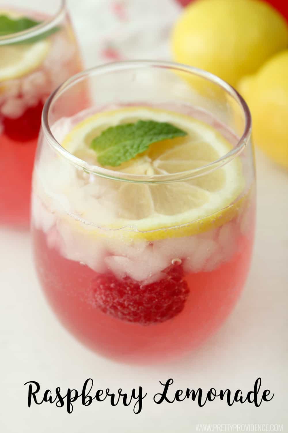 close up of raspberry lemonade in a clear glass with lemons in the background