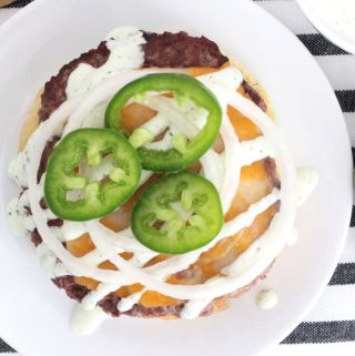 Angus beef patty on a white plate, topped with melted cheese, jalapeño ranch, onions and jalapeño peppers.