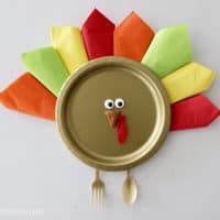 Thanksgiving turkey place setting made with a gold paper plate and colorful napkins.