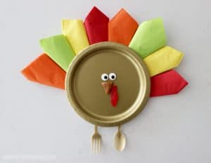 Thanksgiving turkey place setting made with a gold paper plate and colorful napkins.