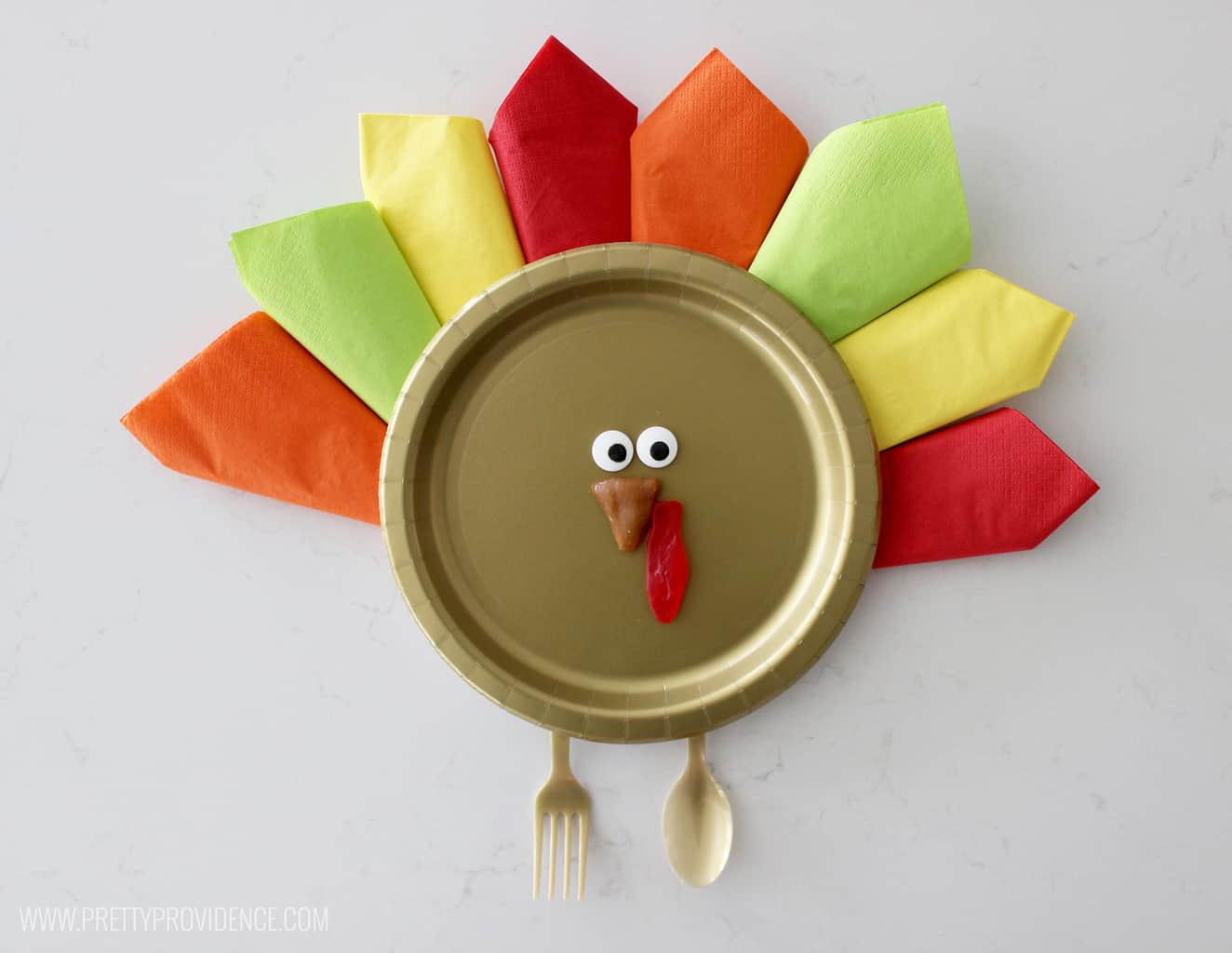 Thanksgiving turkey place setting. Gold paper plate, with napkins folded to look like feathers, fork and spoon for feet and googly eyes.