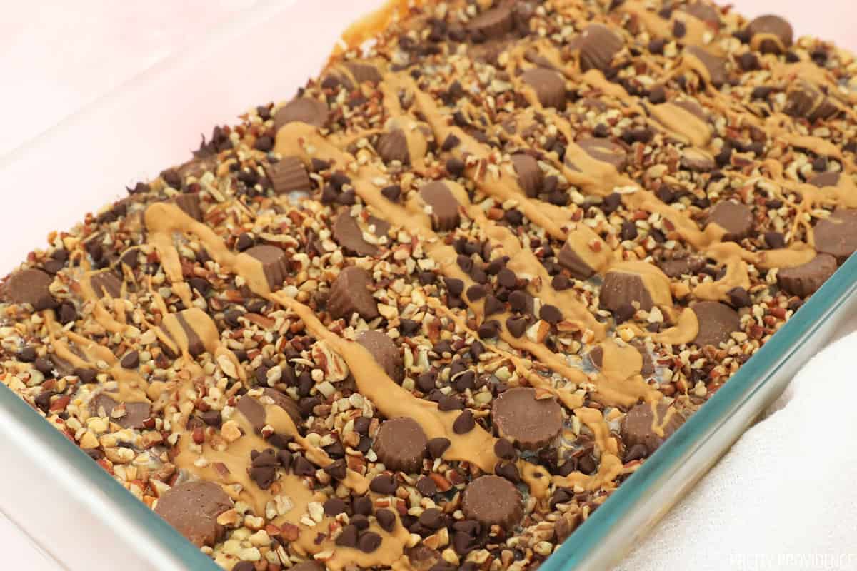 Peanut Butter Magic Bars in a ceramic dish, topped with mini peanut butter cups and drizzled peanut butter.