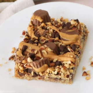 Peanut butter magic cookie bar with mini peanut butter cups, pecan and peanut pieces, mini chocolate chips and drizzled peanut butter on top.