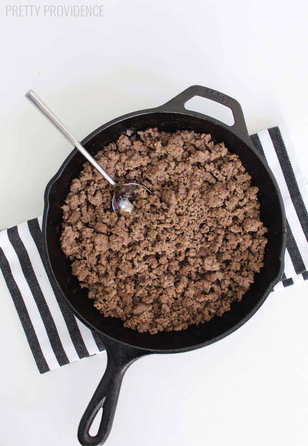 seasoned ground beef in a cast iron pan on a black and white striped towel 