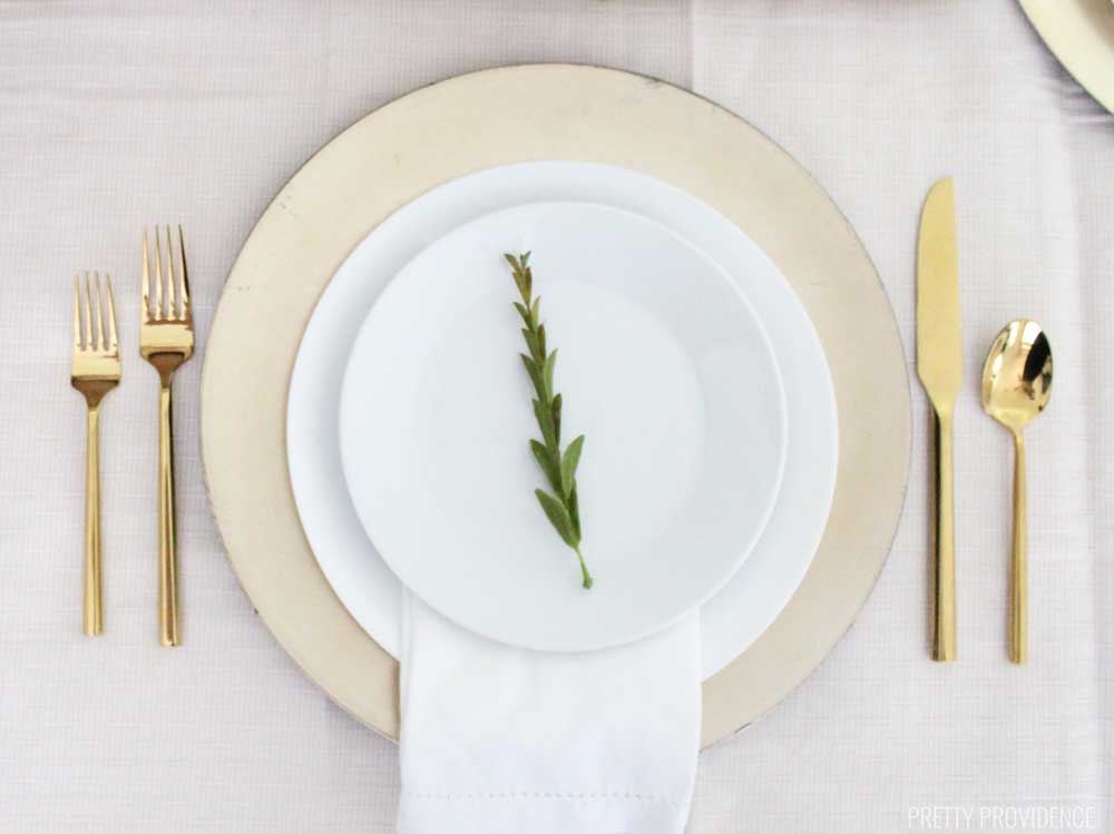 Gold place setting - white plates on a gold charger with a white napkin and a leaf on top of the plates. Classy and simple way to set a table.