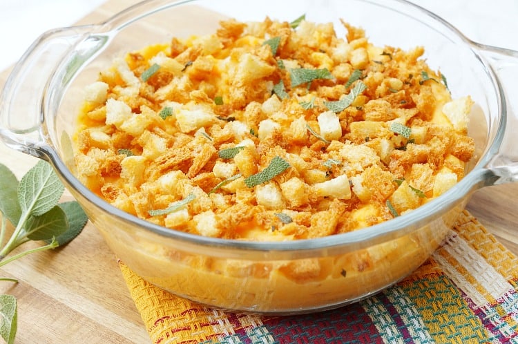 Savory Sweet Potato Casserole in a round glass baking dish topped with fresh sage and breadcrumbs.