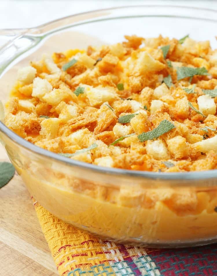 Close up of savory sweet potato casserole in a glass dish with breadcrumbs and sage on top.