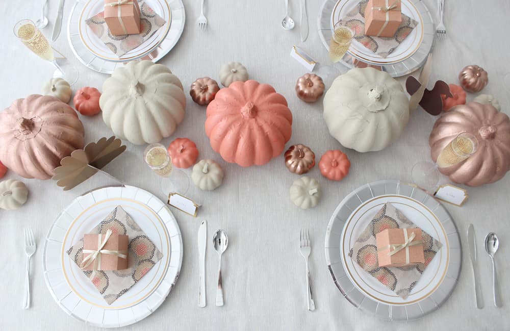 Thanksgiving table overhead view. White plates, silver chargers, orange, cream and copper pumpkins and Thanksgiving favor boxes on each plate.