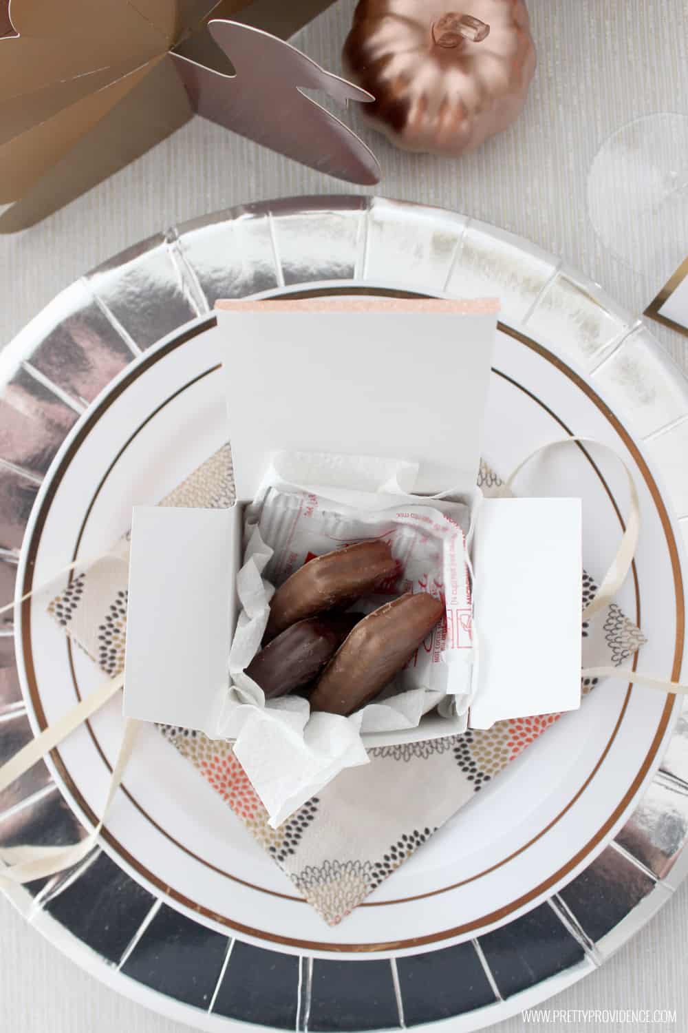 Thanksgiving table setting with silver charger, white plate and a small Thanksgiving favor filled with cookies.