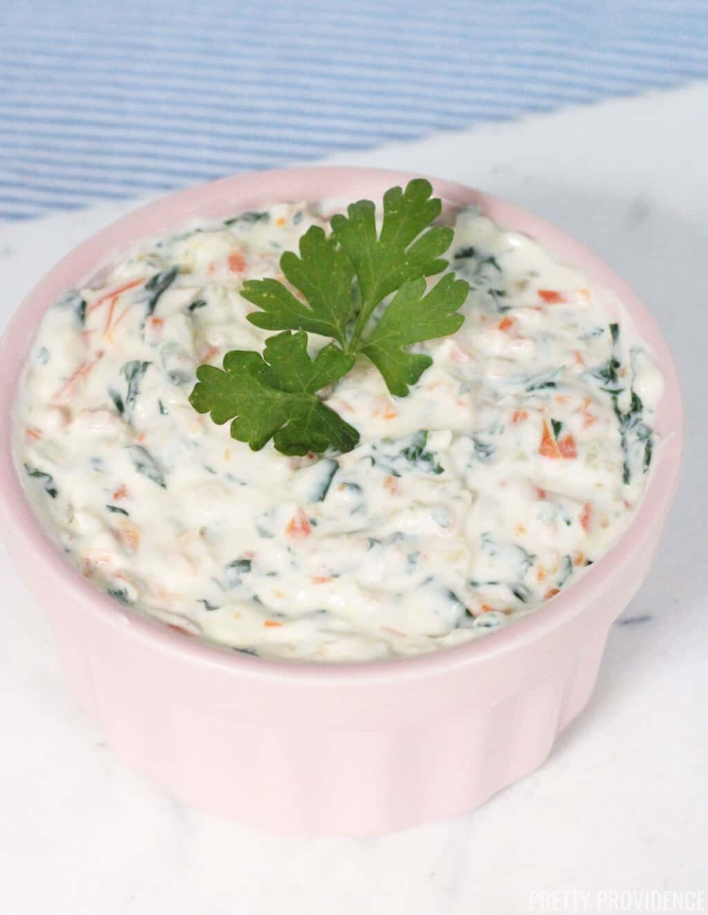 Healthy veggie dip made with yogurt, sautéed vegetables, in a pink bowl and parsley as a garnish.