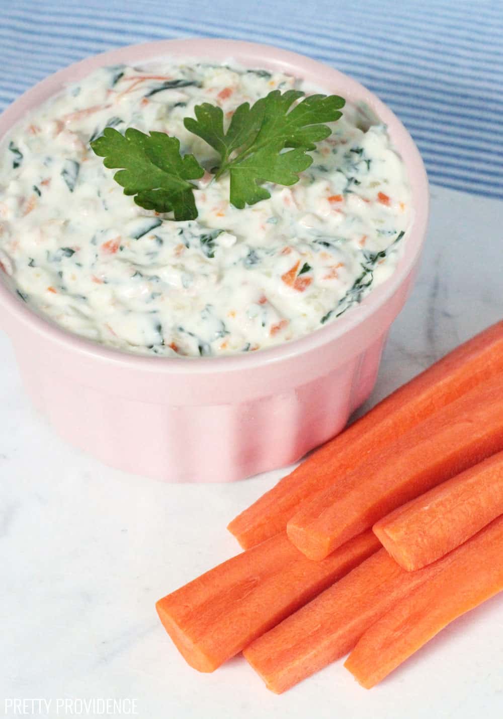Sliced carrots with healthy veggie dip in a pink bowl with parsley as a garnish.