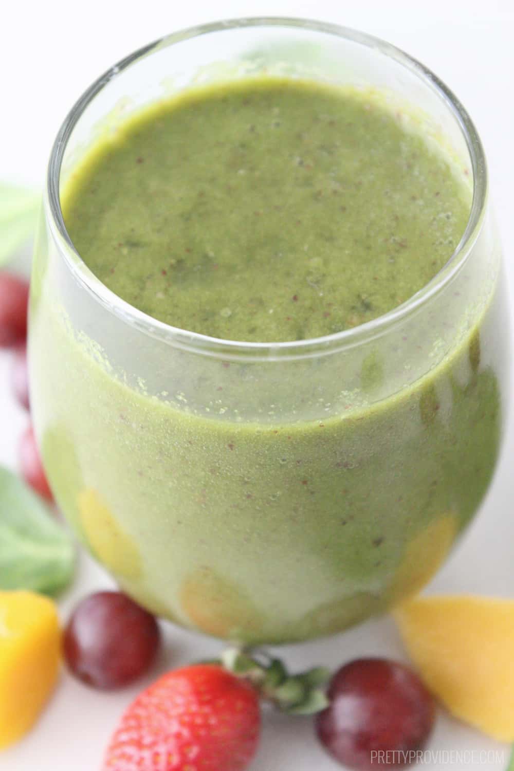 Green Smoothie in a clear glass surrounded by fresh fruit and spinach.