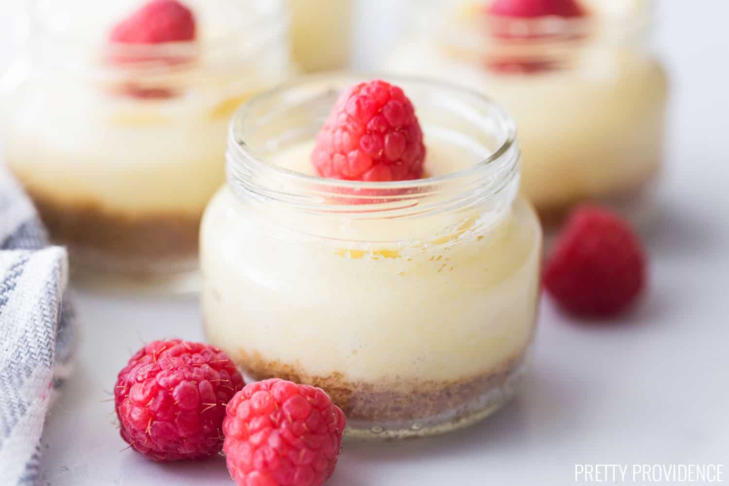 Mini Cheesecakes in jars with raspberries on top.