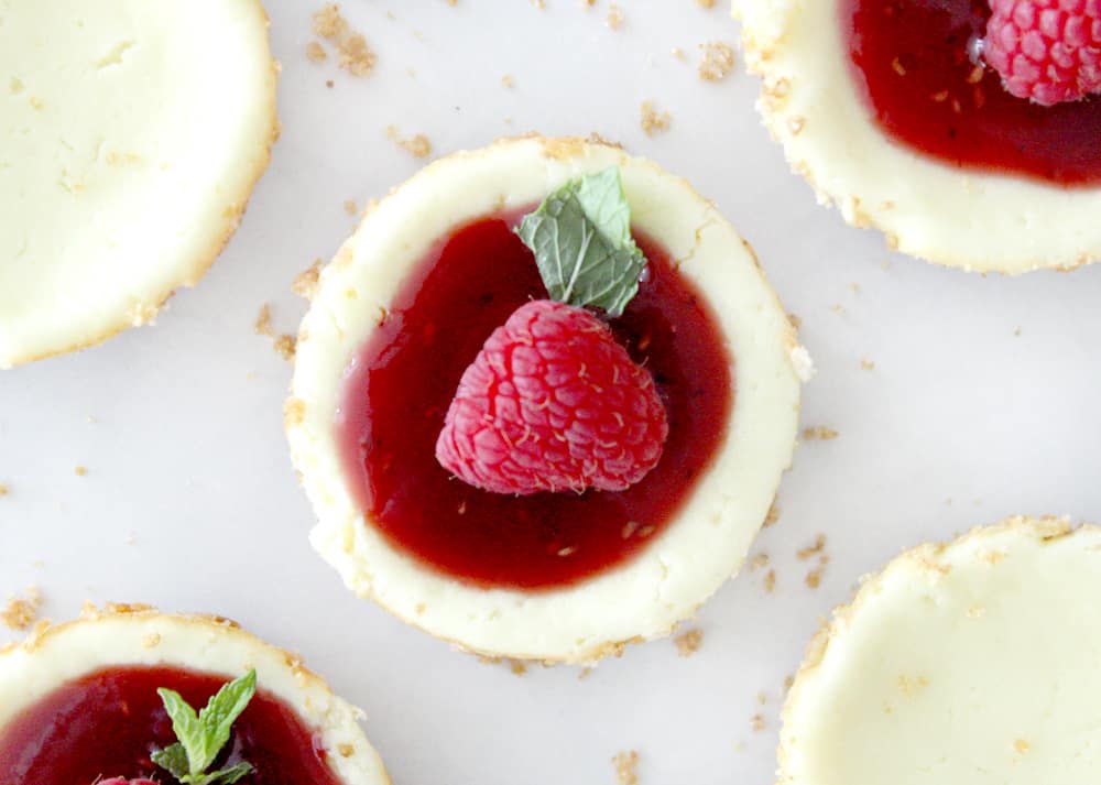 birds eye view of mini cheesecake with raspberry puree, garnished with a raspberry and mint leaf