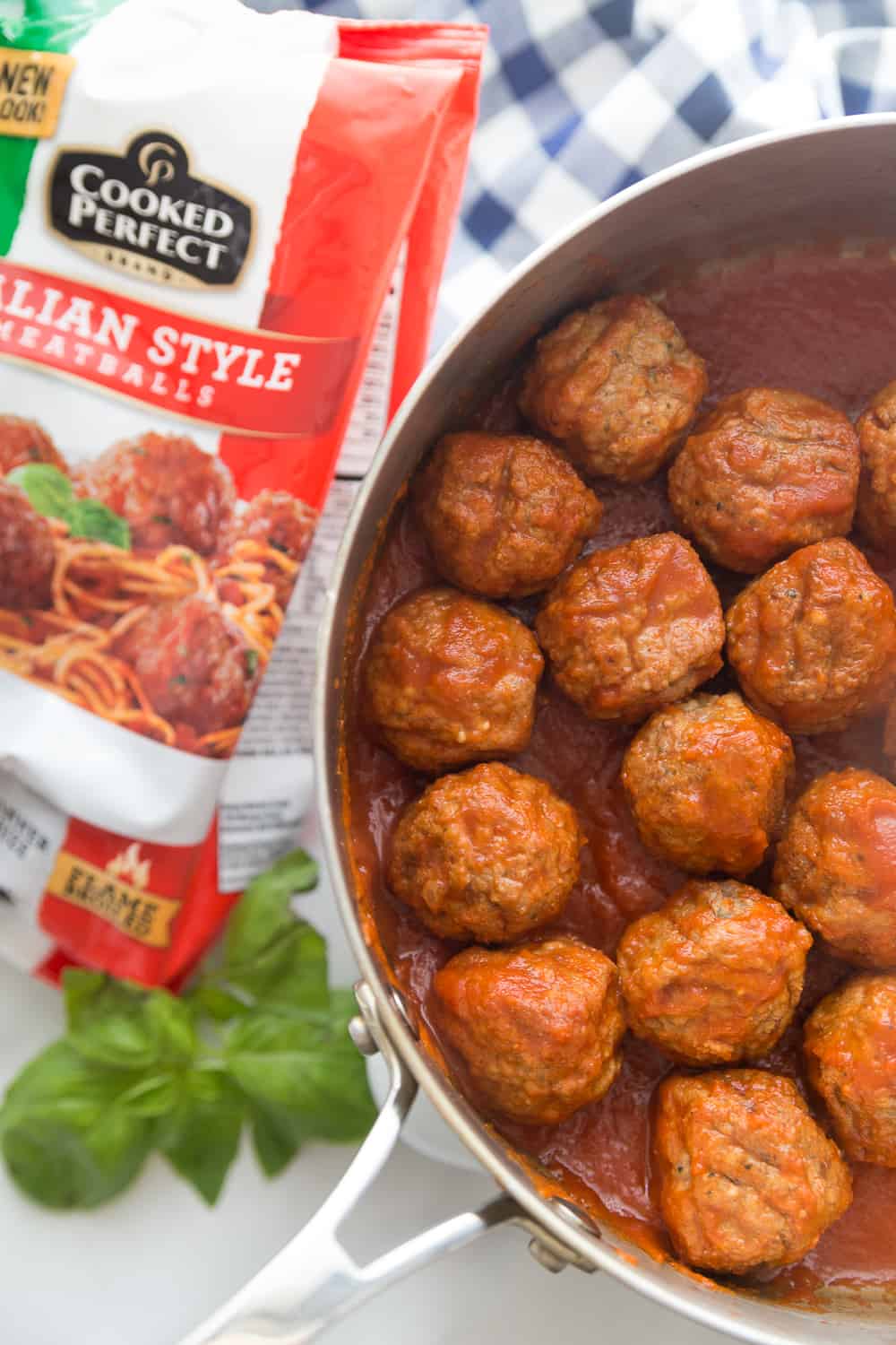 pre cooked meatballs in a skillet next to the package with fresh herbs on the side