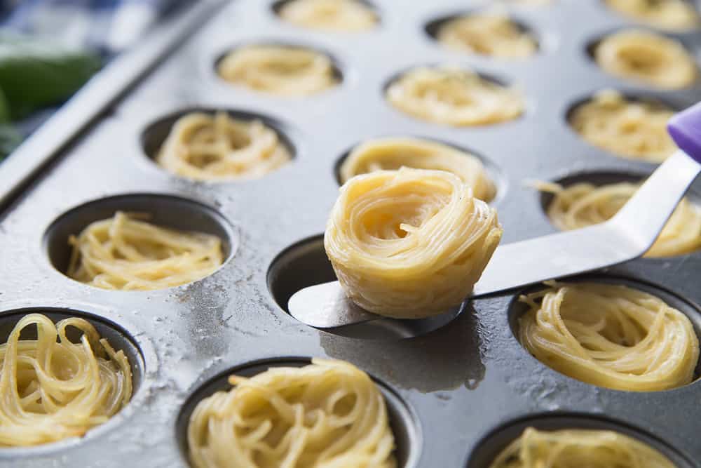 a spatula getting pasta out of a muffin tin 