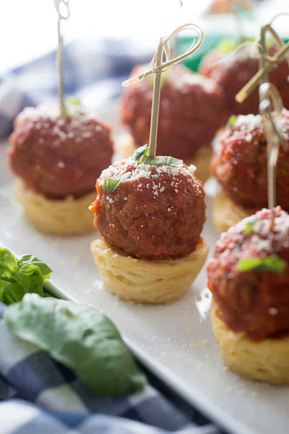 corner of a white platter with mini spaghetti and meatball appetizers on a stick