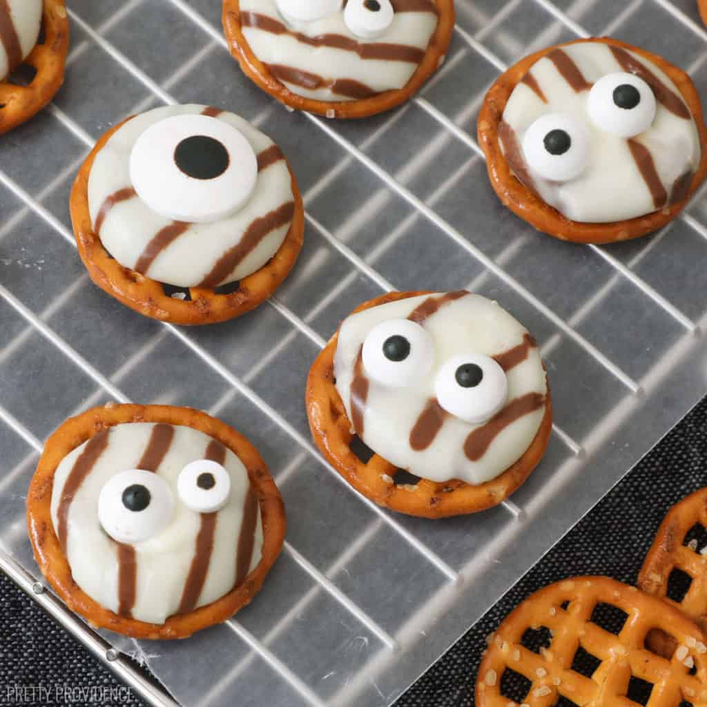 white chocolate striped hersheys hugs melted on to pretzels and topped with candy eyeballs resting on wax paper over a black runner