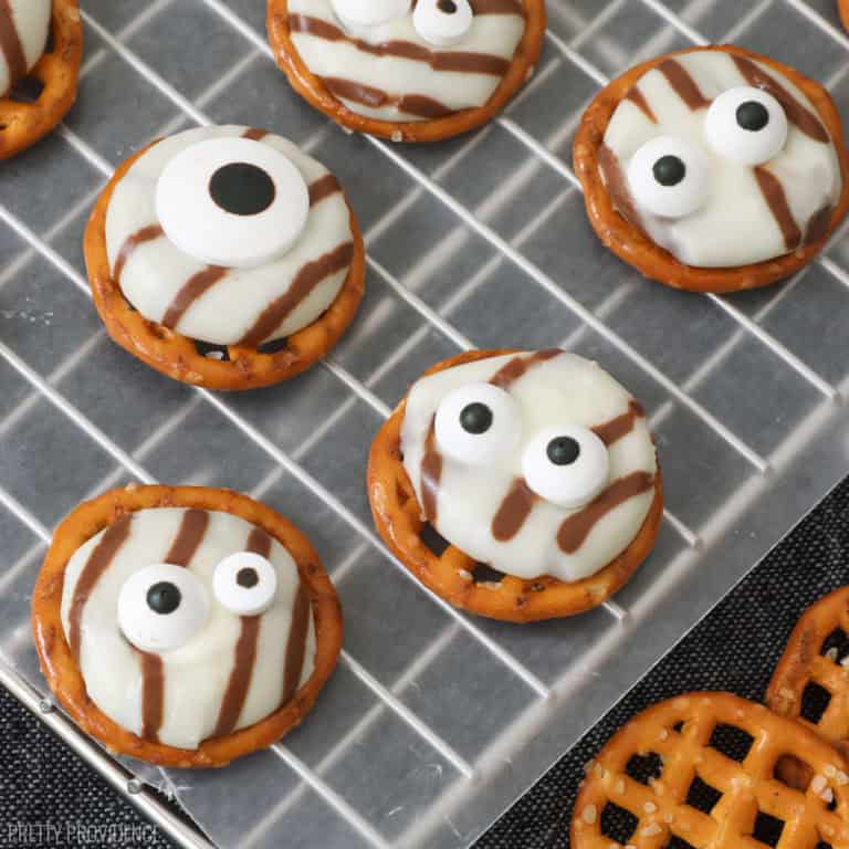 white chocolate striped hersheys hugs melted on to pretzels and topped with candy eyeballs resting on wax paper over a black runner