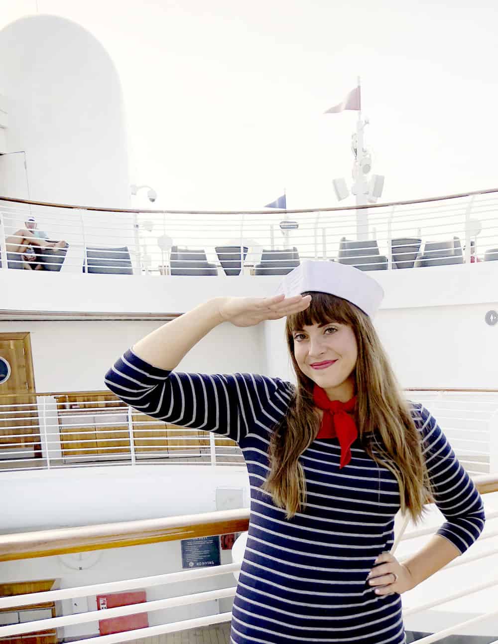 a brown haired girl in a sailor costume saluting on the deck of a ship