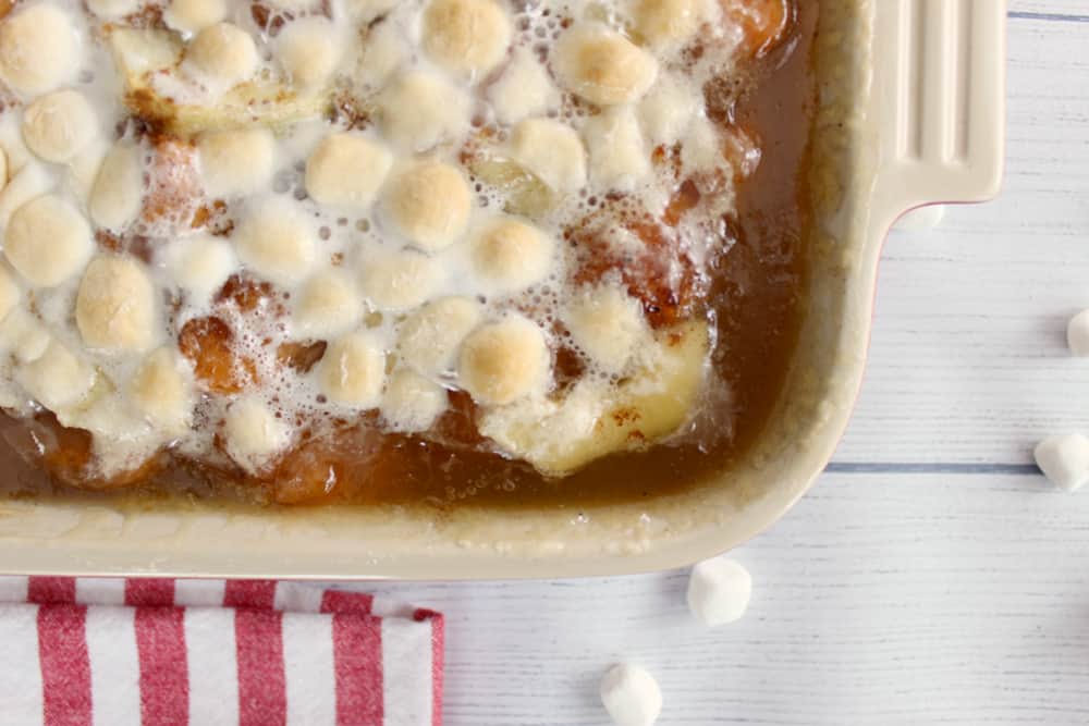 corner of a pan of marshmallow covered sweet potato casserole on a wooden background