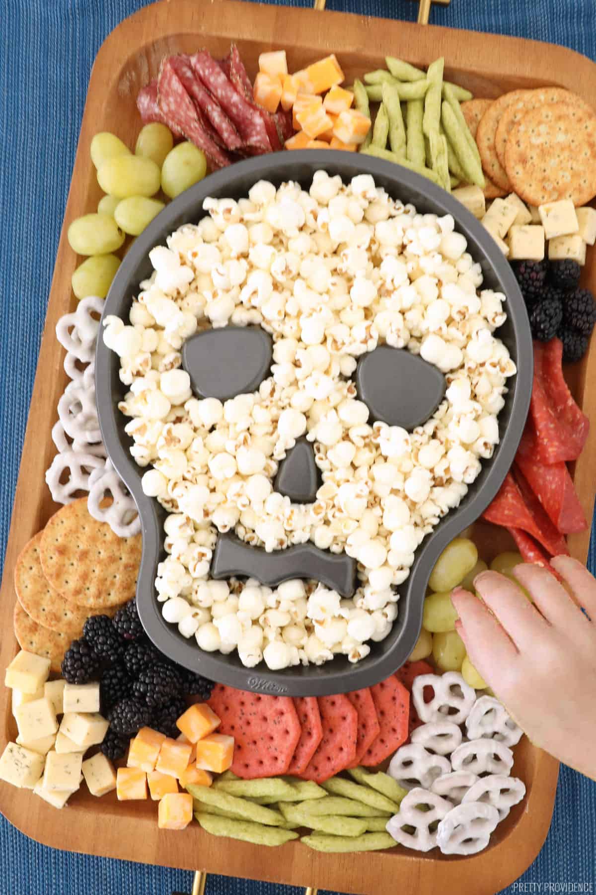 Halloween skull cake pan full of popcorn on a charcuterie board full of  snacks, fruit, meat and cheeses.