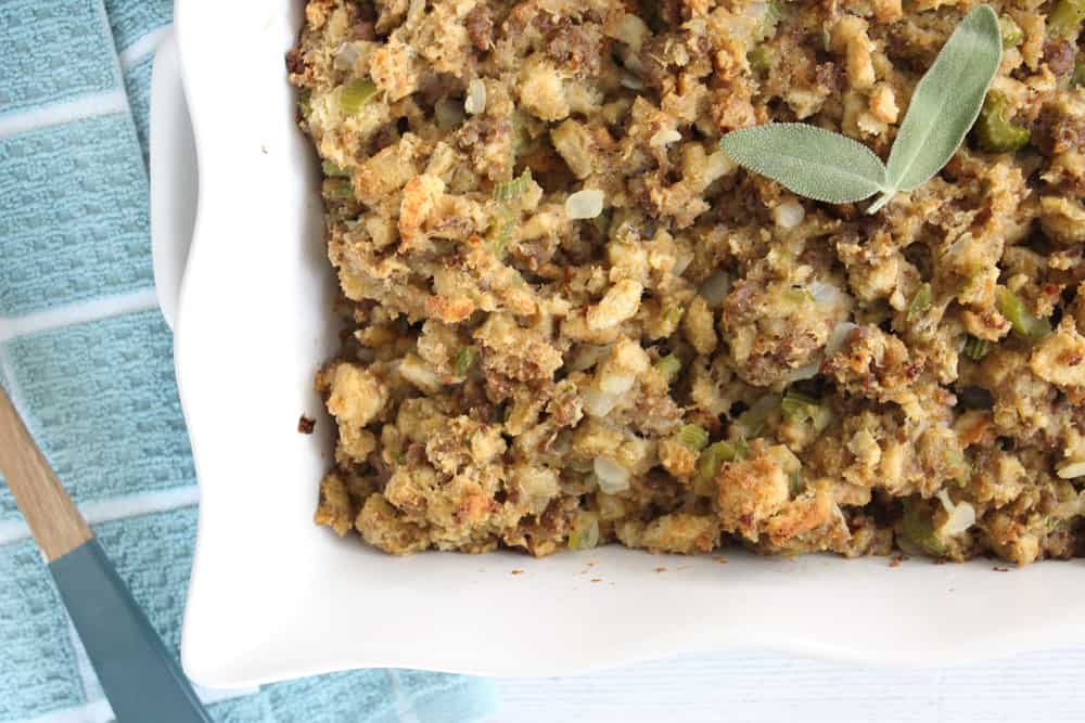 Stuffing with sausage and herbs in a white casserole dish, topped with fresh herb garnish..