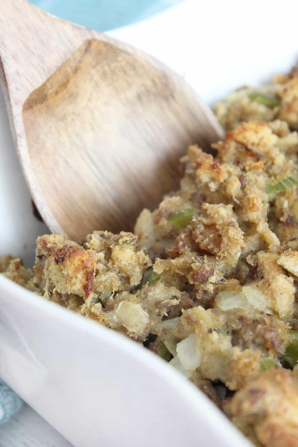 Close up Thanksgiving stuffing in a white casserole dish with a wooden spoon.