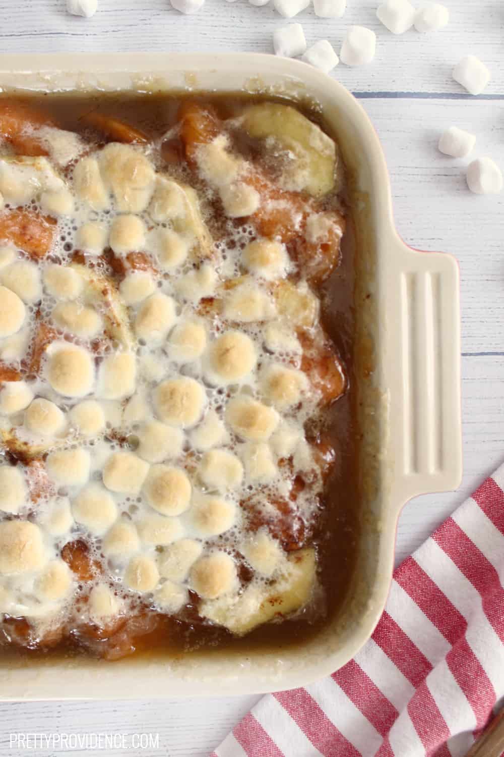 half a pan of sweet potato casserole topped with marshmallows. red and white striped towel in one corner and marshmallows in another