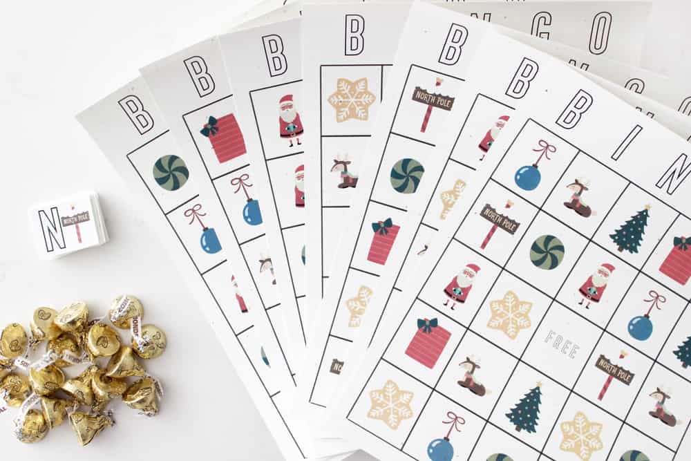 Several printable Christmas cards spread out in a fan next to a pile of chocolate kisses. 