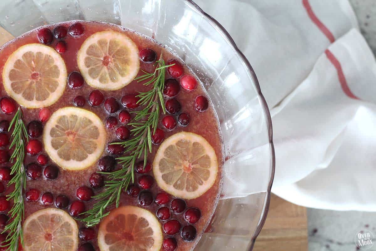 Christmas punch in a glass punch bowl with cranberries, orange slices and sprigs of rosemary in it.