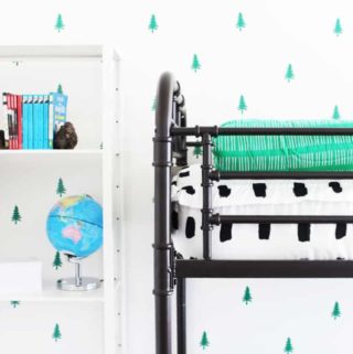 A white wall with green DIY wallpaper made of little trees with a bunk bed and shelf in front of it.