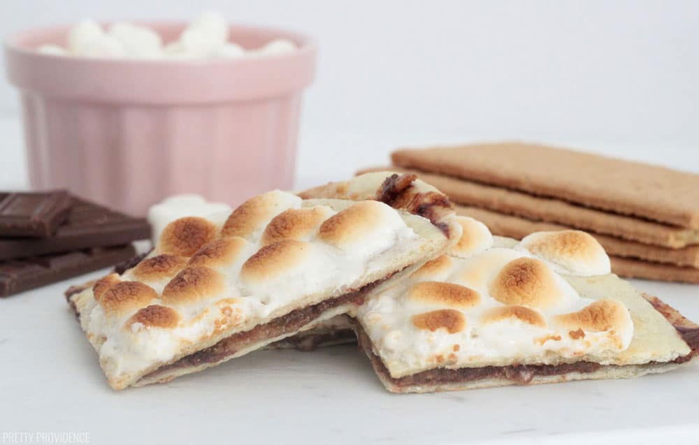 Triangles of S'mores Dessert Quesadilla topped with toasted marshmallows, with graham crackers, Hershey bars and marshmallows in the background.