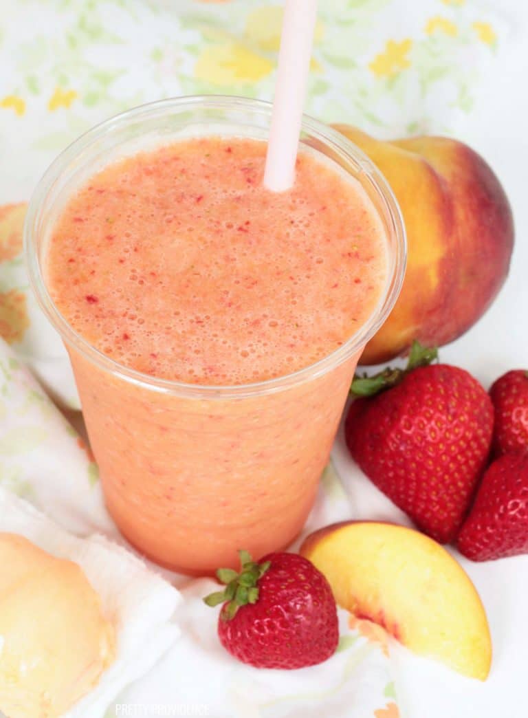 Caribbean Passion smoothie with peach slices, strawberries and a pink straw as garnish.