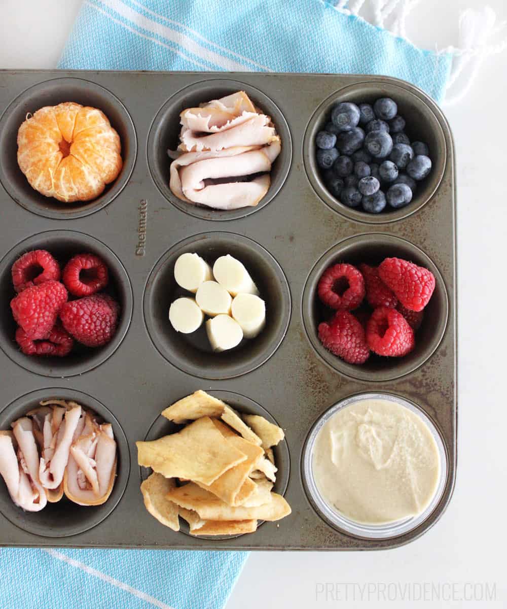 Muffin Tin Lunch, an orange, turkey, blueberries, raspberries, chips and hummus in a muffin tin.