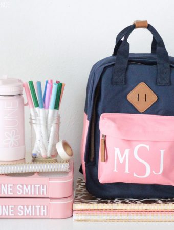 Personalized Kids Backpack, water bottle, and lunch boxes on top of notebooks. Jar of markers and washi tape.