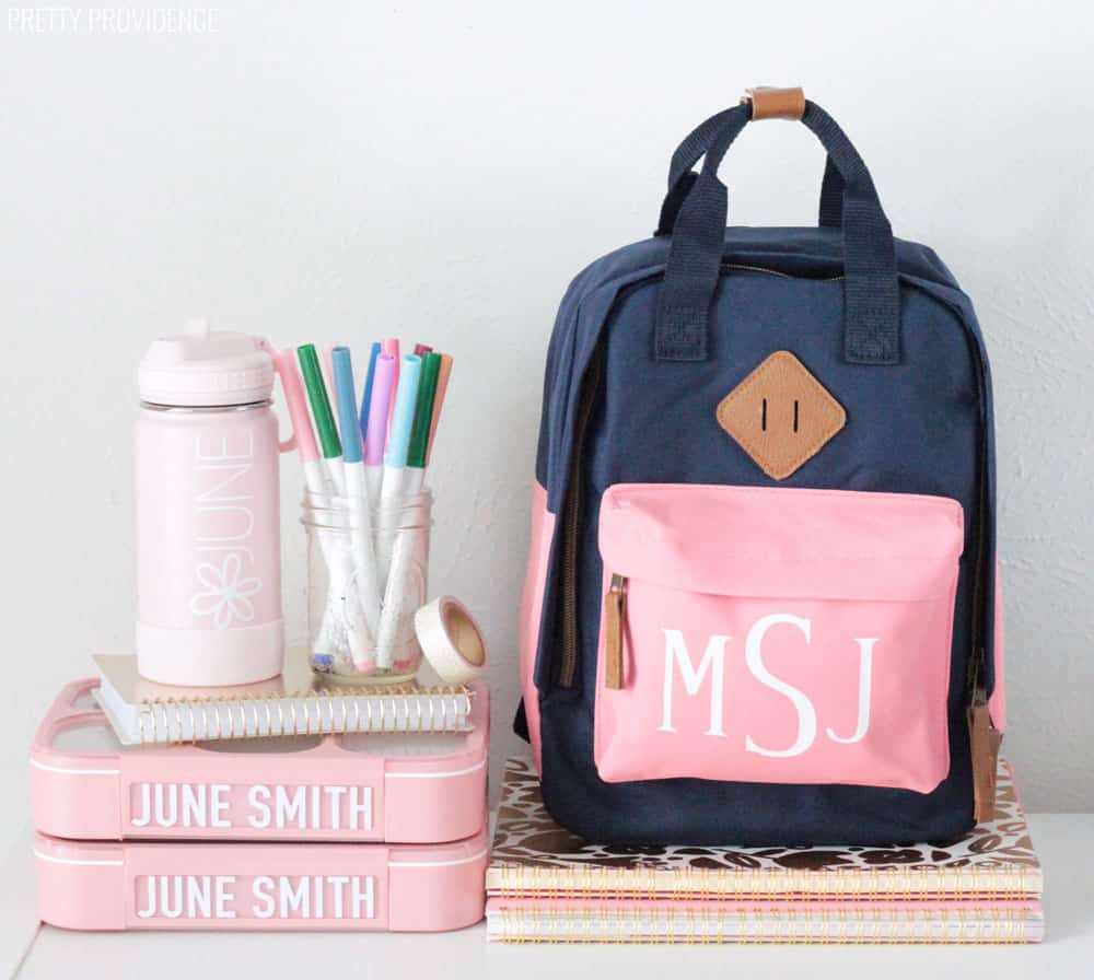 Personalized Kids Backpack, water bottle, and lunch boxes on top of notebooks. Jar of markers and washi tape.